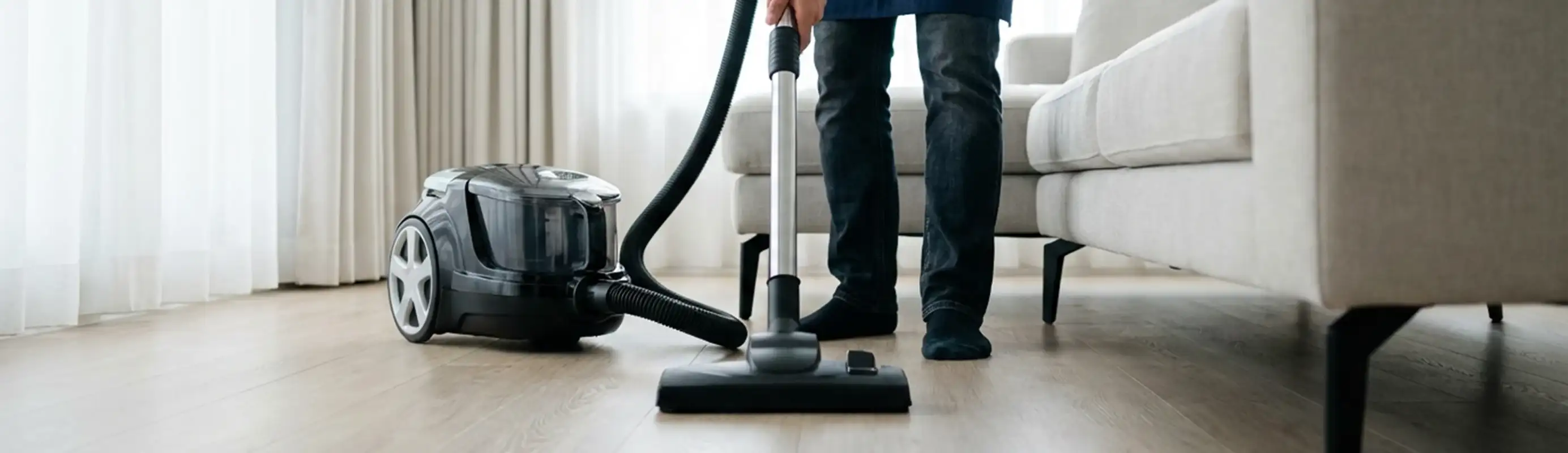 Professional house cleaner vacuuming a living room floor with a canister vacuum cleaner, Jacksonville, FL.