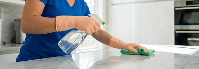 Maid service worker spraying and wiping a kitchen countertop with a microfiber cloth for sanitizing, Jacksonville, FL.
