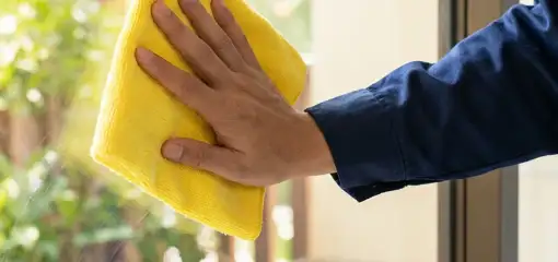 House cleaner wiping a glass window with a yellow microfiber cloth for streak-free cleaning, Jacksonville, FL.
